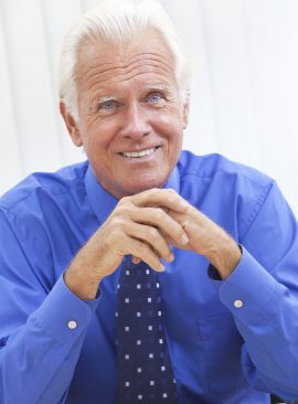 A smiling senior male medical doctor looking happy at his desk in an office at a hospital